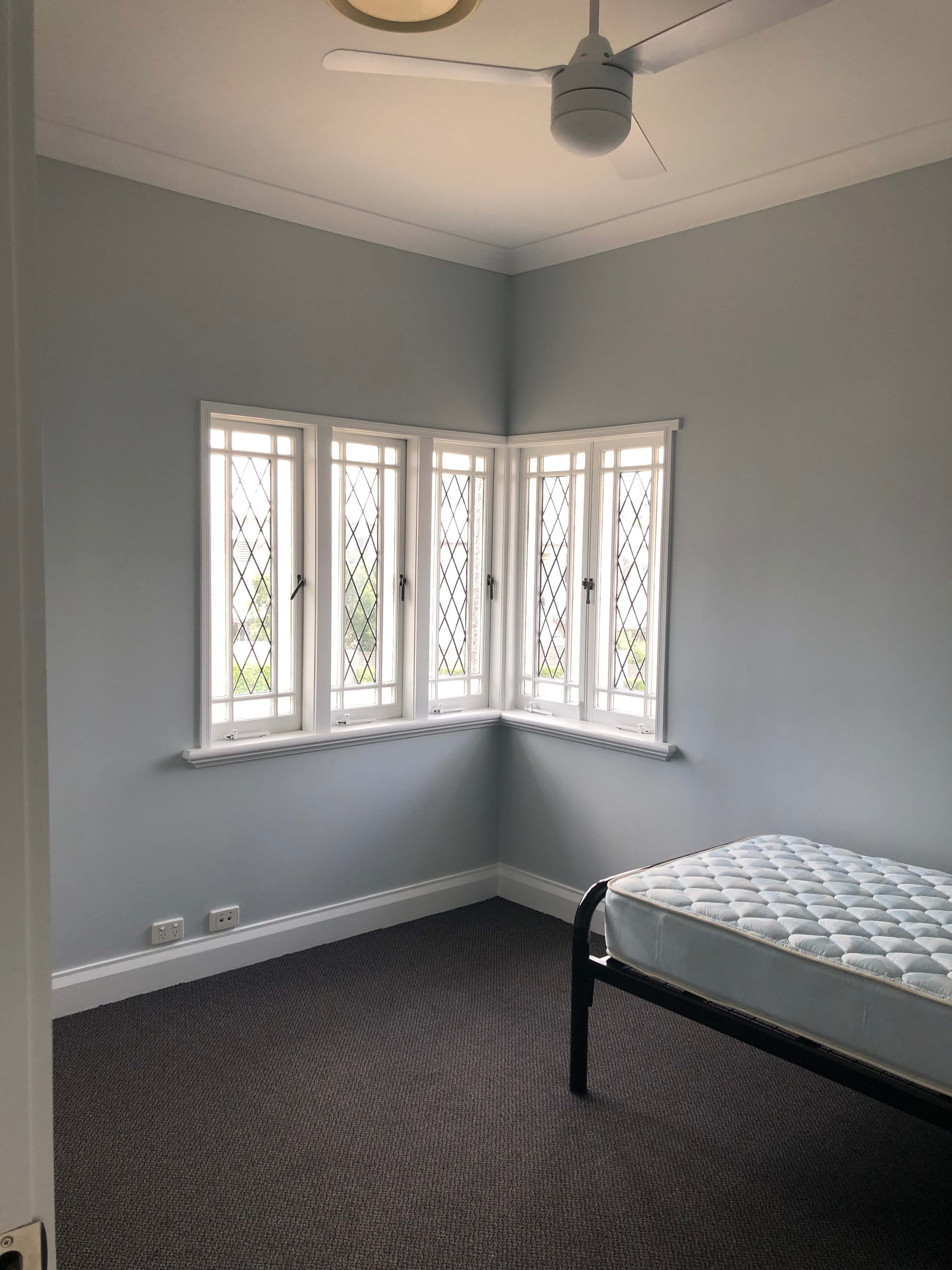 completed building maintenance in Brisbane view of newly refurbished bedroom interior view from door single bed against walls with corner window and ceiling fan 